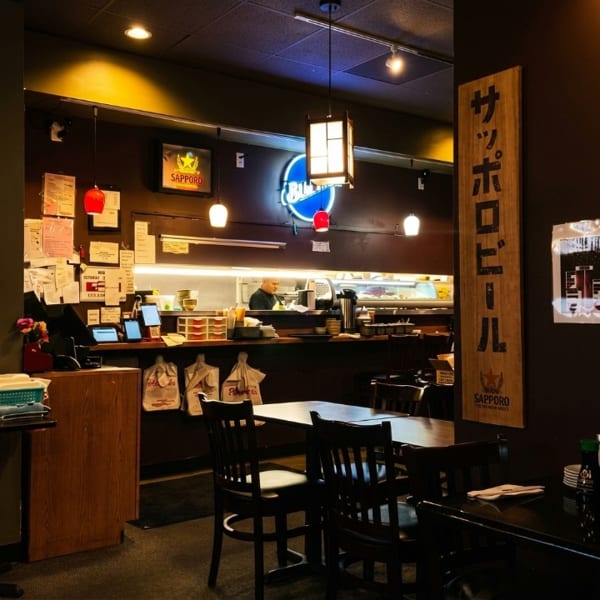 Interior of a Japanese restaurant with a sushi bar, chef, and dining tables.