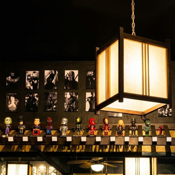 Superhero bobbleheads and black and white movie posters adorn a dark wall with a hanging lantern.
