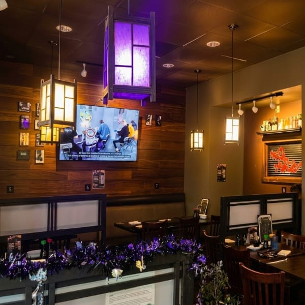 Restaurant interior with wooden walls, booths, tables, a TV, and purple and white lanterns.